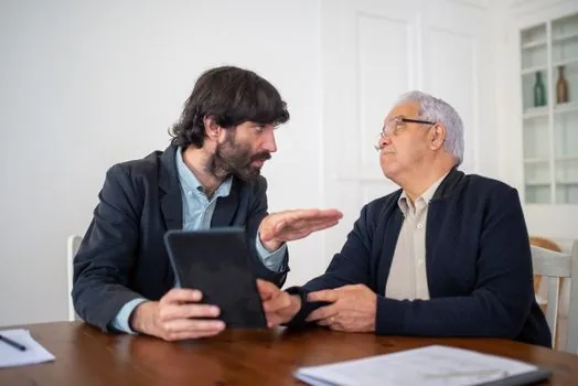 Elderly parent and adult child consulting at community service provider desk with voucher approval notice and calendar, warm realistic Korean welfare office photo | 제공기관 계약 상담 | 선정 통지 뒤 등록 제공기관과 이용일정을 정하는 장면