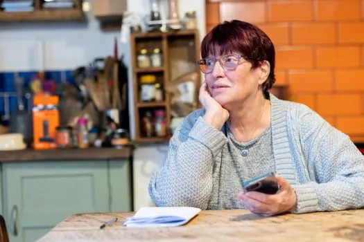 Korean adult child reviewing elderly parent's smartphone bill and welfare discount memo at kitchen table, clear daylight, realistic photo