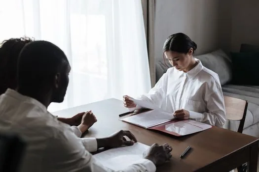 Korean family reviewing hospital discharge papers and medical benefit documents with social worker, bright realistic consultation room