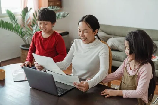 Korean family sorting veteran certificate application documents, government website on laptop, ID card and file folder on table, warm daylight realistic photo | 확인서와 등록신청 구분 | 제출처가 요구한 증명서명과 보훈 등록 여부를 먼저 확인하는 장면