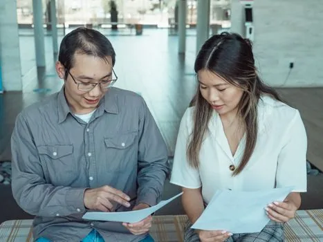 Korean senior parent and adult child reviewing welfare card, car registration certificate and parking placard application at community center counter, realistic documentary photo | 주민센터에서 장애인 주차표지 신청서와 복지카드를 확인하는 장면 | 발급 대상과 준비서류를 설명하는 이미지