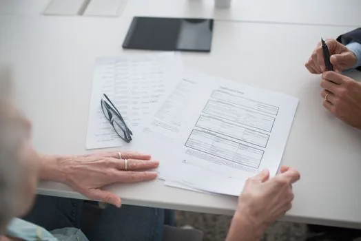 community service center consultation desk with driver's license return application form and pen | 행정복지센터에서 면허 반납 신청 준비물을 확인하는 장면