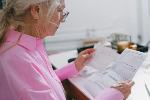 Korean adult child checking elderly parent's welfare eligibility certificates and family relation document at home desk, warm daylight, realistic photo | 산림복지서비스이용권 신청 전 복지 자격과 가족관계 서류를 확인하는 장면